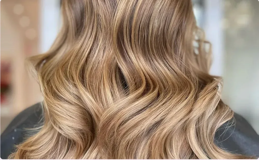 Sunlit caramel-blonde waves, showing the movement keratin extensions keep when they are cared for.